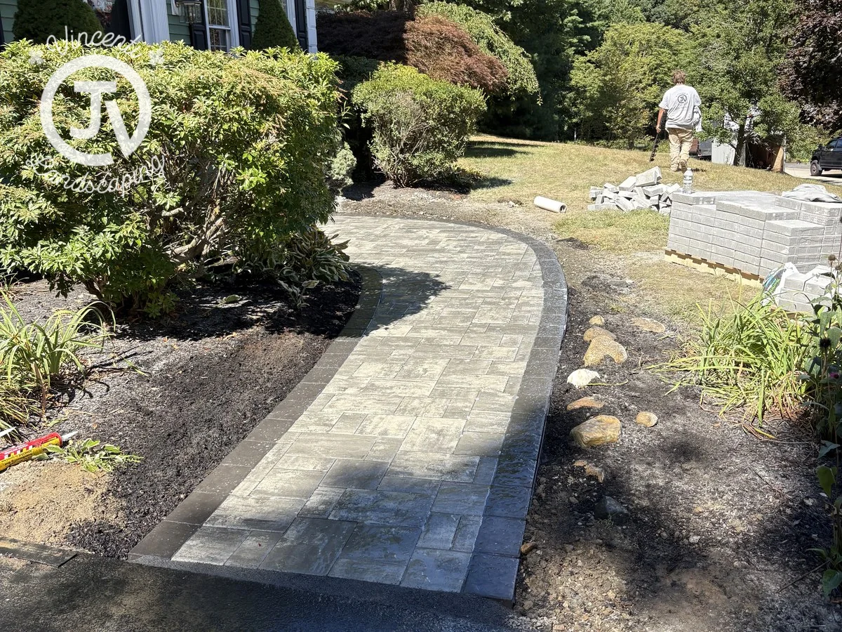 Curved gray paver walkway with a dark border during installation by Vincenti Landscaping