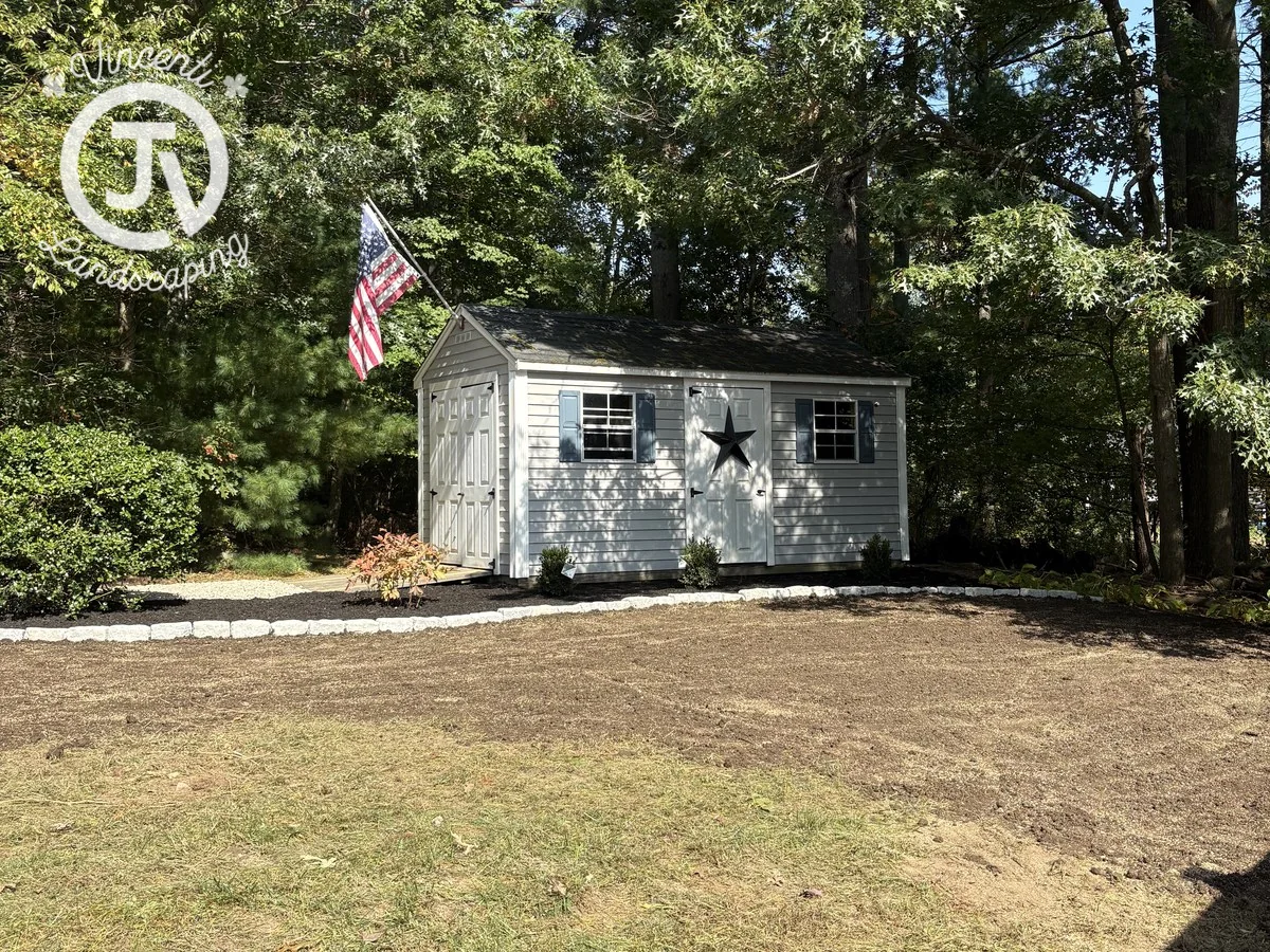 After: white shed bordered by stone edging and freshly mulched planting beds installed by Vincenti Landscaping