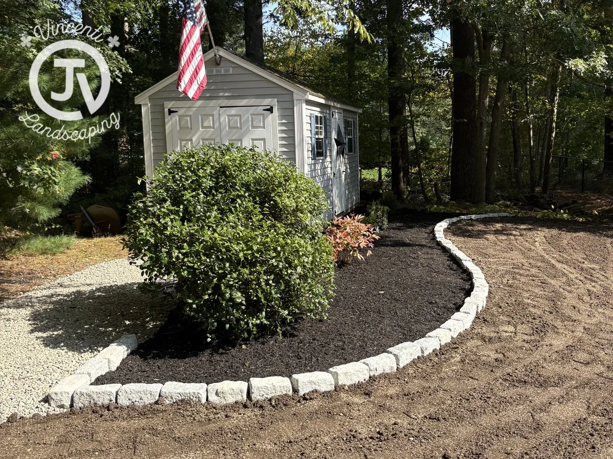 Curved stone edging separating a freshly mulched shed planting bed from prepared soil